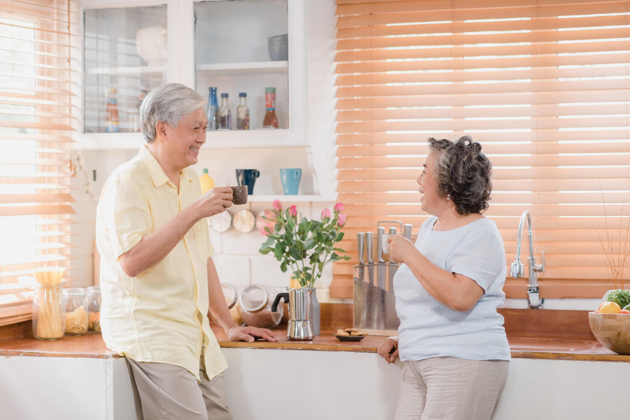 Asian elderly couple drinking warm coffee and talking together in kitchen at home. Chinese couple enjoy love moment while taking together at home. Lifestyle senior family at home concept.