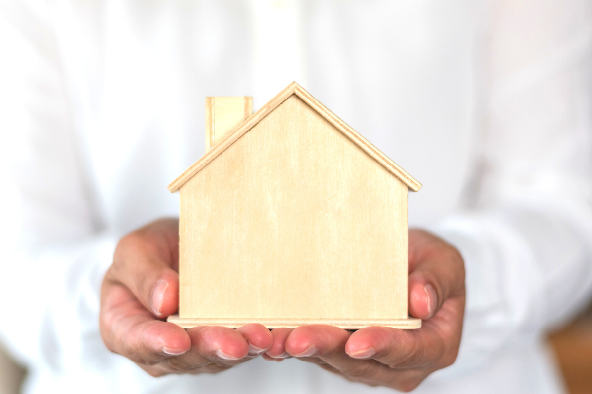 A person in a white dress shirt caringly holds a wooden house in their hands as a property management cares for properties.