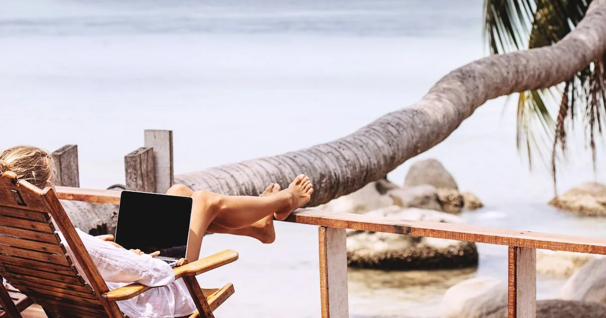A woman works on a laptop at the beach after embracing remote landlordship.