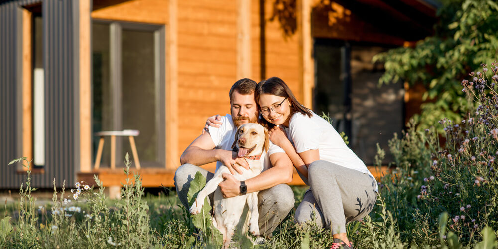 Portrait of a young couple hugging happy dog sitting on the backyard of their wooden country house