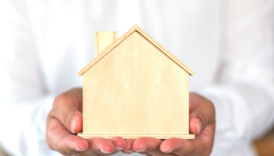 A person in a white dress shirt caringly holds a wooden house in their hands as a property management cares for properties.